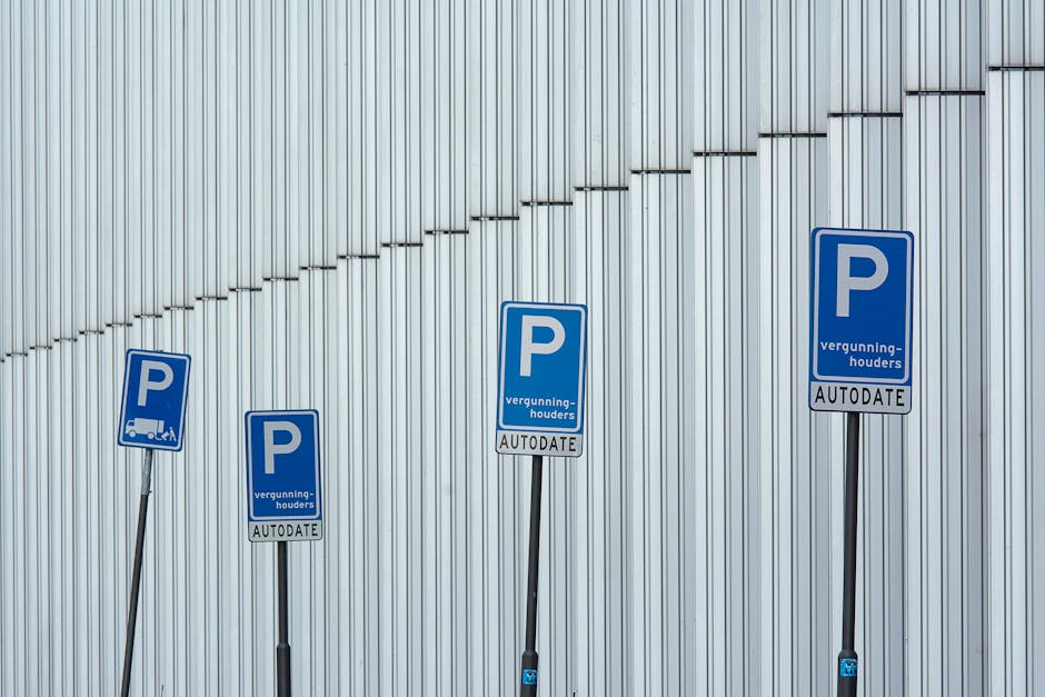 Four blue parking permit signs with white 'P' symbols are mounted on slanted black metal poles against a background of a metallic wall with vertical panels. The signs display the words 'vergunninghouders' and 'AUTODATE' beneath the 'P' symbols. The signs are positioned at varying heights from left to right, with the tallest near the right side. The metallic wall behind features evenly spaced vertical lines, adding a textured appearance with subtle shadows. This image illustrates parking permissions that may be relevant for home relocations or moving services by Man with Van Riddlesdown, highlighting the importance of parking permits during the process of furniture transport and loading in residential or commercial areas.
